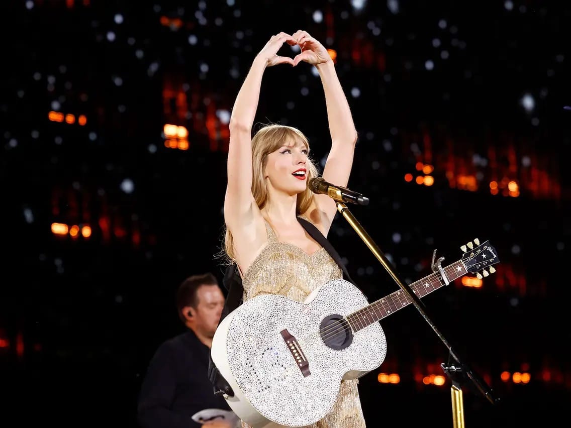 Taylor Swift makes a heart hands gesture to fans at a concert.