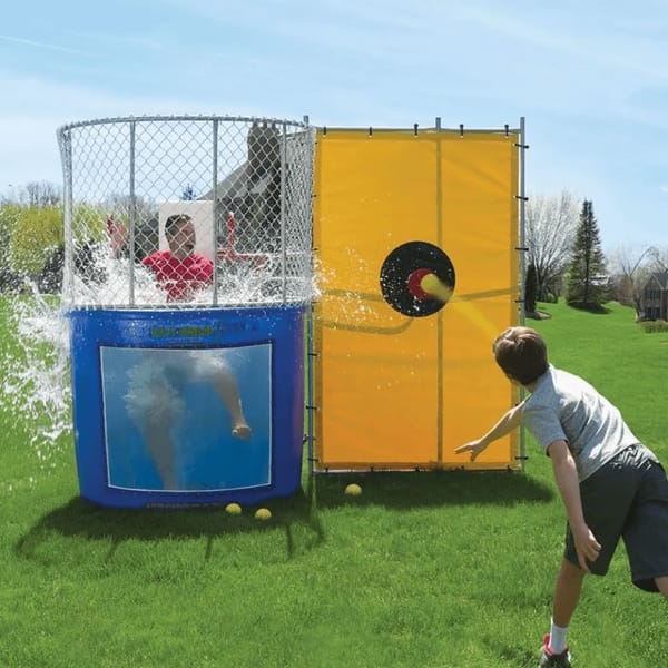 Person throws a ball at a dunk tank, sinking a person wearing a red shirt into the water.